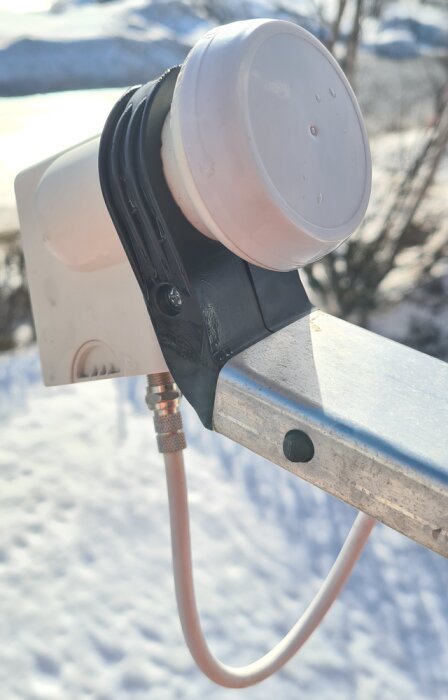 LNB fäst på en parabolarm med en koaxialkabel ansluten mot en snöig bakgrund, visar tätt fäste och armens orientering.