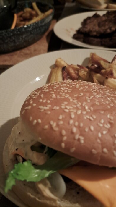 Närbild av en hamburgare med sesambröd, grönsaker och ost, serverad med pommes frites.