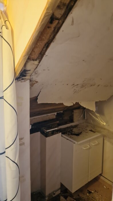 Vattenskada i tak och vägg, blöta fläckar och skadat köksskåp i hus.
