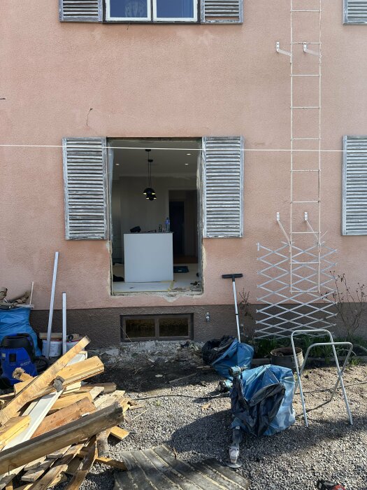 Installation av nya dubbelglasdörrar i fasaden på ett hus under renovering, med byggmaterial och stegar framför.