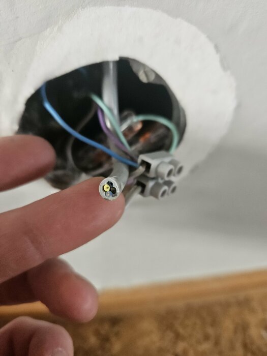En person pekar på en öppen elektrisk dosa med flera kablar i väggen.