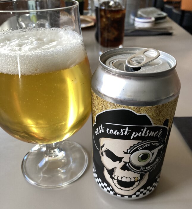 Ett glas med West Coast Pilsner och en öppen burk, minimal skumkrona.