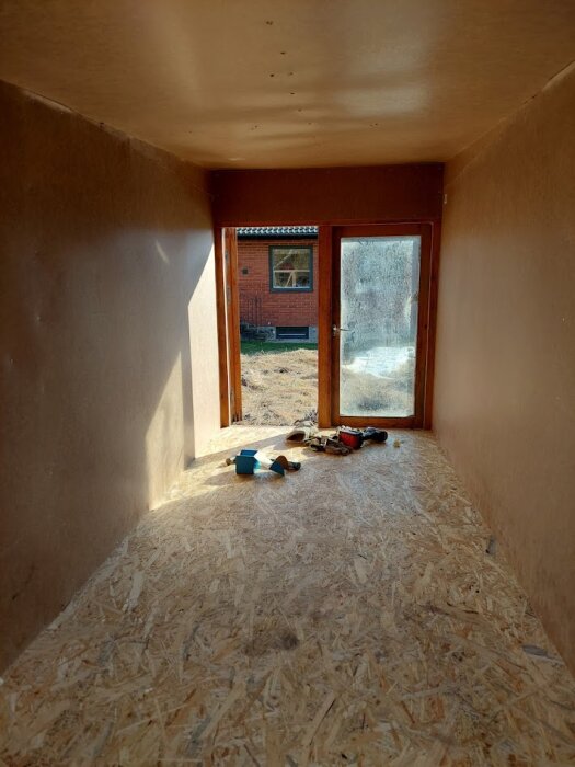 Interiör av en regelstomme med oljehärdad masonit, isolering, målade väggar och plastmatta på golvet.