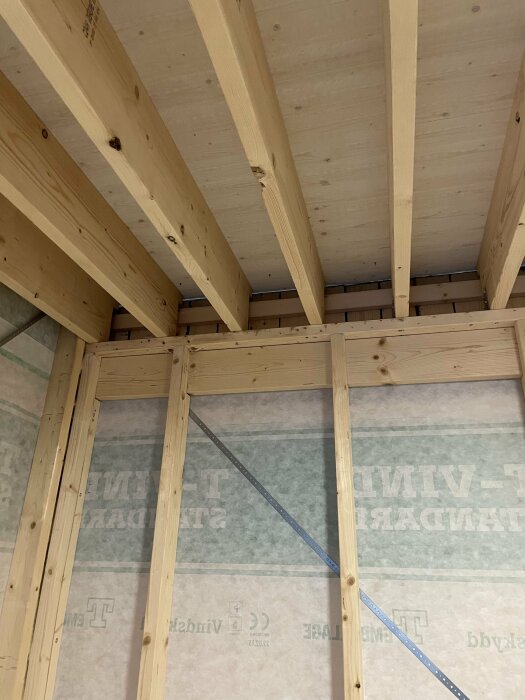 Konstruktion av ett nytt förrådstak med synliga träbjälkar och partiell isolering mellan takstolarna.
