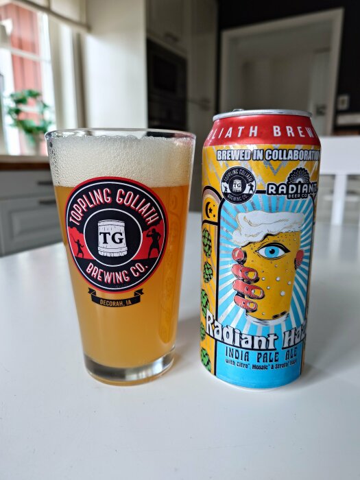 Ett glas öl med skum bredvid en konstnärligt designad ölburk på ett köksbord.
