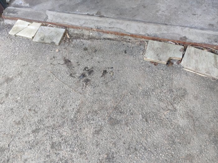 Bild på en betongyta med sprickor bredvid en garageinfart, där några plattor lyfts upp för att visa djupet.