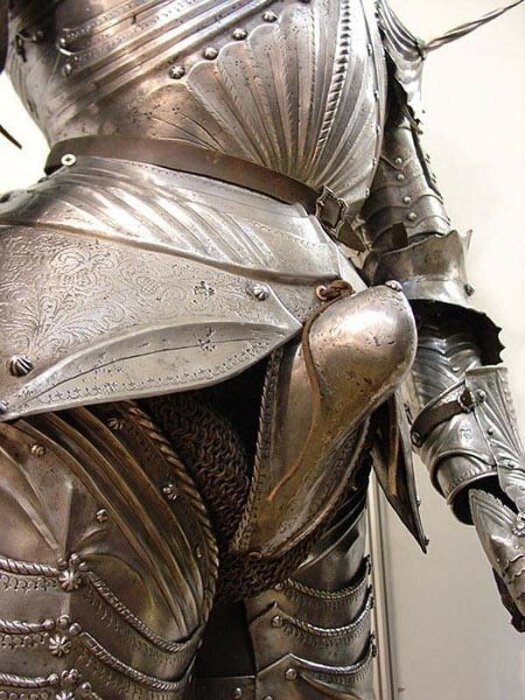 Närbild av dekorerad medeltida rustning med visir, bröstplåt och armpansar.