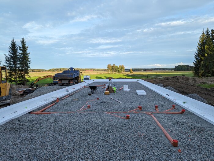 Grundarbete med rörsystem och kantelement för bostadshus under uppbyggnad, i naturskönt landskap.