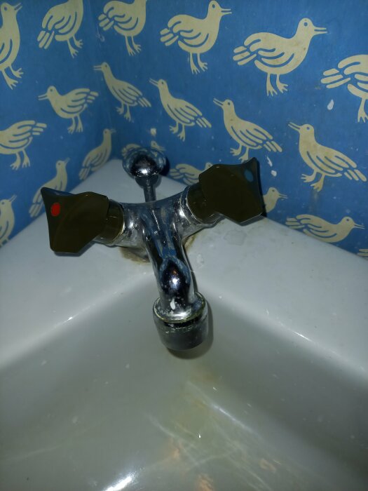 Kromad kran med röd och blå markering som droppar, okänd modell, mot bakgrund av tapet med fågelmotiv.