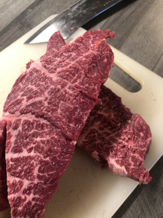 Högrevskött med marmoreringsdetaljer på skärbräda nära en kökskniv.