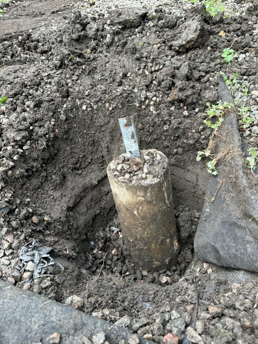 Spade som gräver upp ett betongrör ur marken, svårt att få bort, jord och sten runtomkring.
