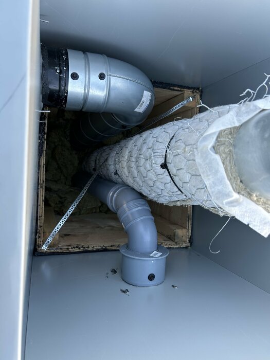 Ventilationssystem med flexibel slang kopplat till en vägggenomföring och en extra ventil bredvid en stormkåpa i ett byggprojekt.