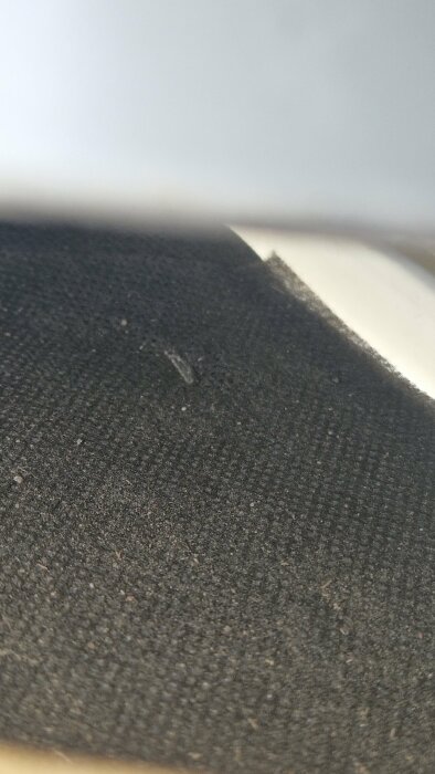 Närbild av en nit under en plåt med svart textilbakgrund.