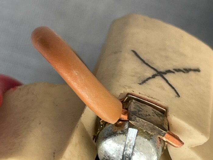 En orange kabel markerad med X i tusch ansluten till en äldre elektrisk kontaktpunkt.