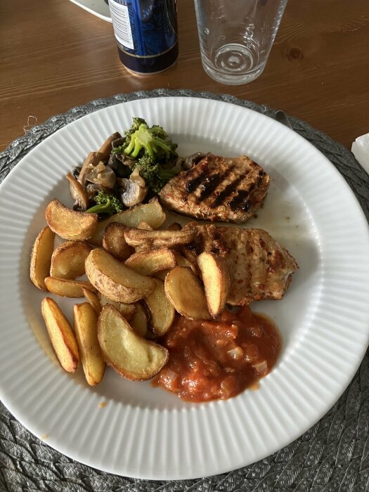 Grillade chilimedaljonger med potatisklyftor, broccolimix, lök och svamp samt pizzasås på en vit tallrik.