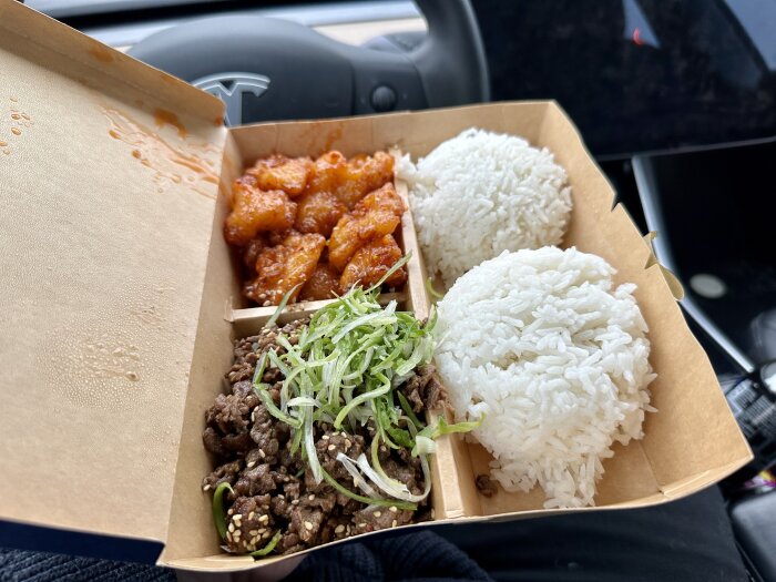 Öppen takeout-låda med ris, koreansk beef bulgogi och kyckling i bil.
