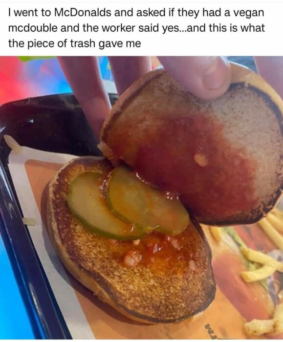 Bröd med tre pickle-skivor och ketchup, på McDonald's serveringsbricka, förmodligen ett missförstått veganalternativ.