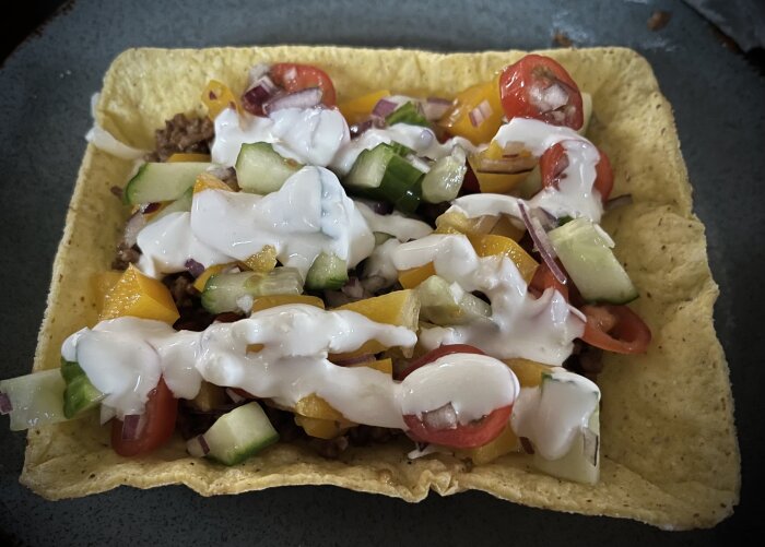 Taco med fyllning av grönsaker, köttfärs och vitlöksdressing på en tallrik.
