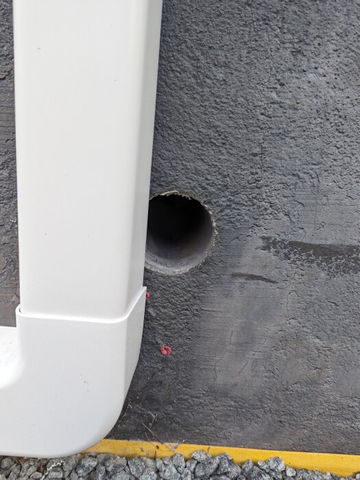 Ett nytt hål genom en grå vägg vid marken med rörledning intill, för en luft/luft pump installation.
