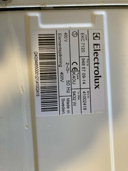 Produktetikett på en vit Electrolux-apparat visar modell EKC7120, 400V elementspänning och tillverkad i Sverige.