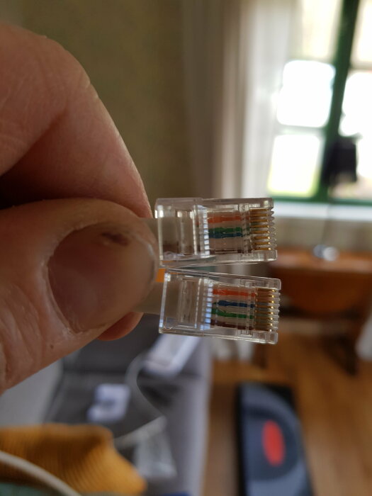 Hand håller två Ethernet-kablar med RJ45-kontakter för att jämföra kabelordning, felaktig ordning överst.