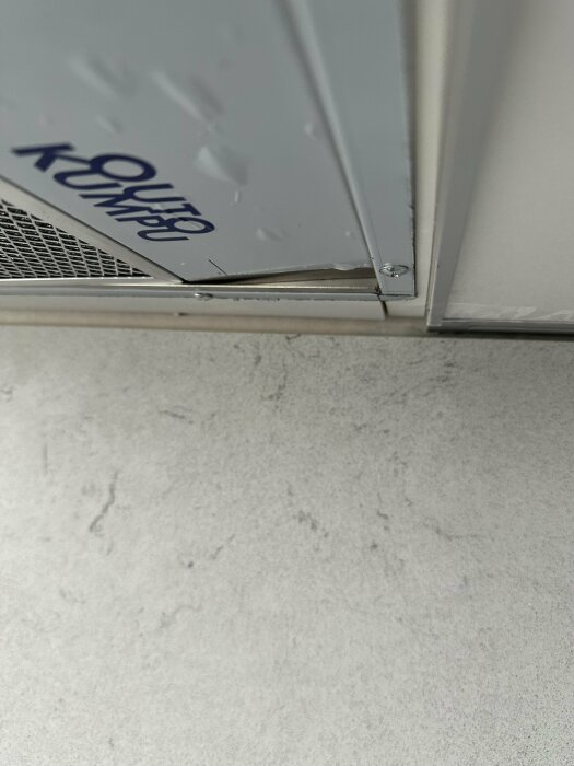 Glipa mellan överkant av ljusgrå väggskiva och vita skåp utan silikonfog, synlig skruv och märket Nerostein.