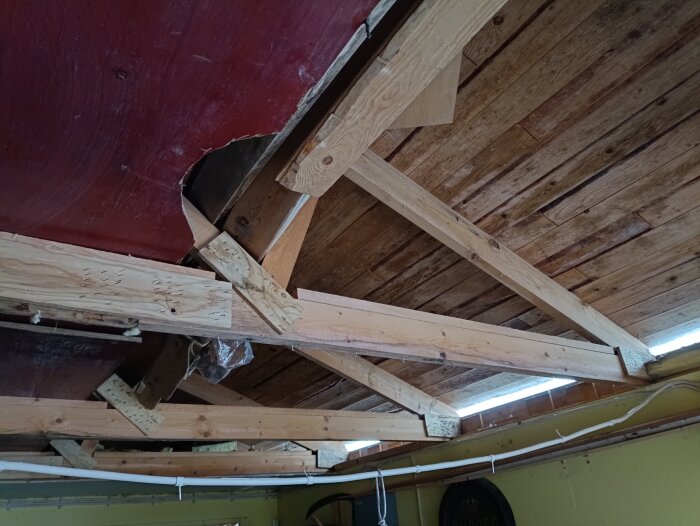 Delvis rivet innertak i garage med synliga träbjälkar och skadade isoleringsrester under taket.