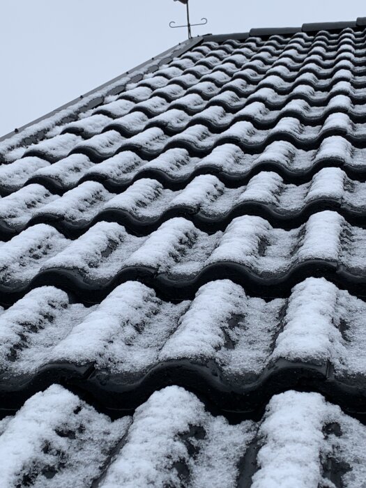 Snötäckt Benders betongtak med synliga läktskikt, mot husets takfot.