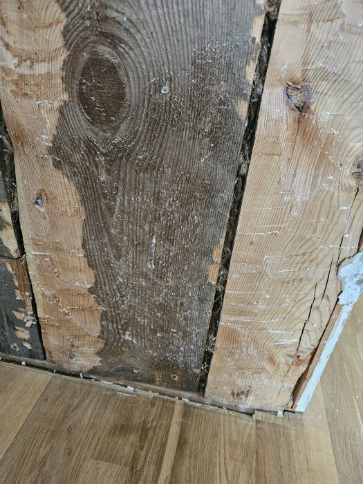 Detaljbild av en hörnsektion där en grov träbalk möter en annan i en innervägg, synliga årsringar och spikar.
