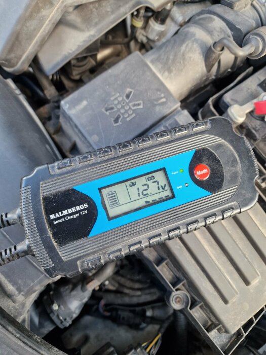 Batteriladdare ansluten till ett bilbatteri visar spänning på 12,7 volt.