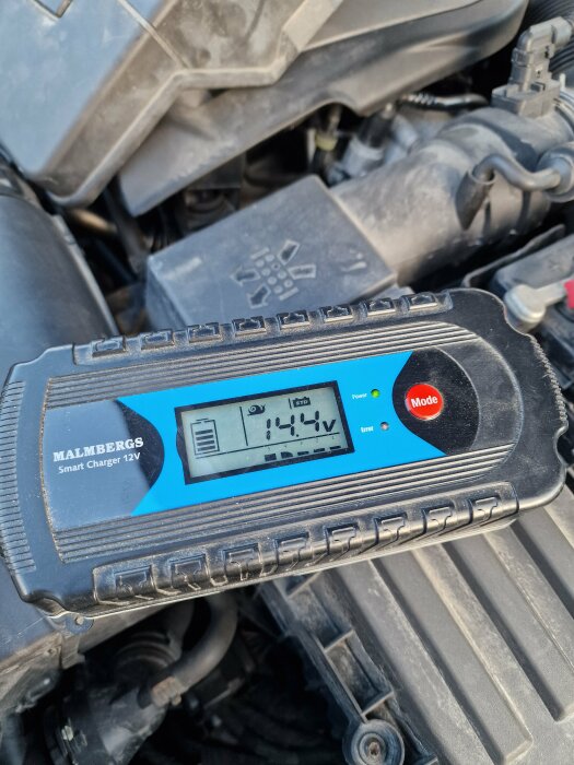 Batteriladdare visar 14,4V placerad på ett bilbatteri under motorhuven.