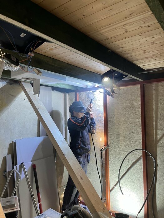 Person som svetsar fyrkantsprofil till väggförstärkning inne i ett hus under renovering.