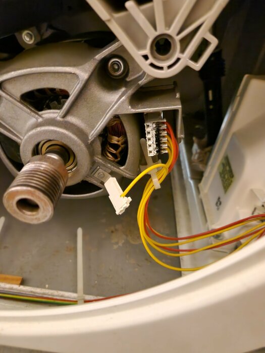 Insidan av en tvättmaskin med synlig motor, drivrem och elektriska anslutningar.