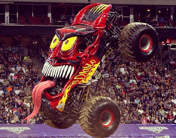 Monstertruck med röd och svart demon-tema i luften framför publik.