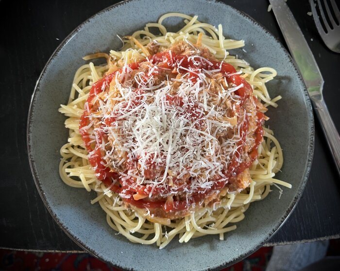 Tallrik med spaghetti och köttfärssås toppad med riven parmesan, synliga grönsaker.