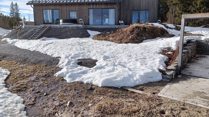 Utsikten från platsen för framtida pool: smältande snödrivor och husfasad.