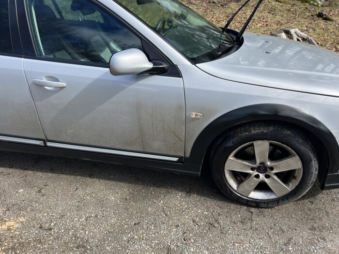 Bil som visar vintersmuts på sidan och smutsiga fälgar, behöver tvätt och underhåll.