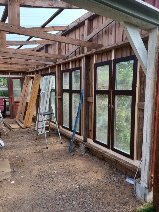 Ombyggnad av gammalt garage till växthus med liggande råspont och glasfönster, byggmaterial syns.