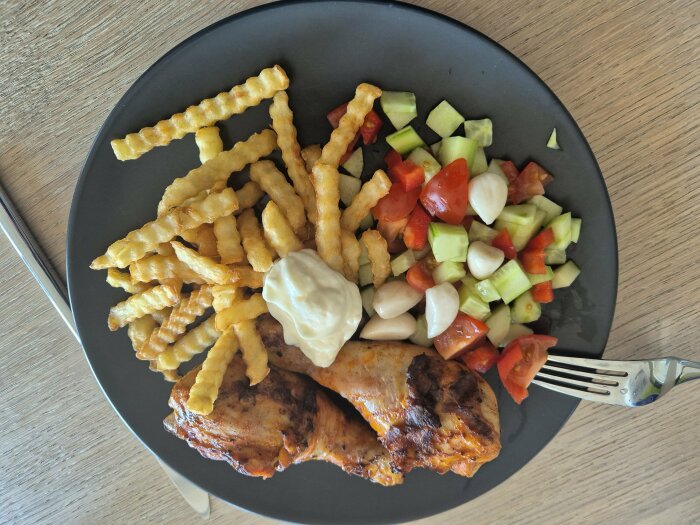 Grillad kyckling med krispiga franska potatisar och en fräsch grönsallad på en svart tallrik.