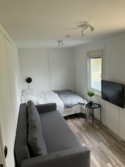 Litet renoverat rum med soffa, säng, tv på väggen och en takfläkt, indikerar behov av ventilationsoversyn.