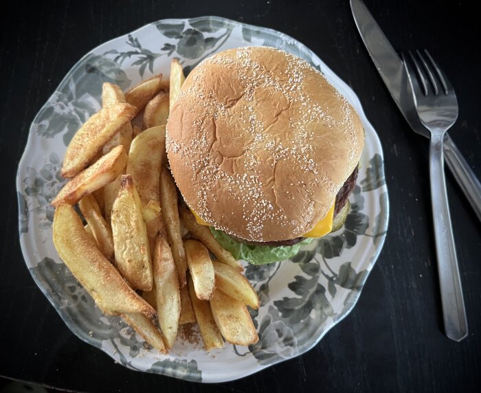 Hamburgare med ost och specialcoleslaw, serverad med pommes frites på ett mönstrat fat.