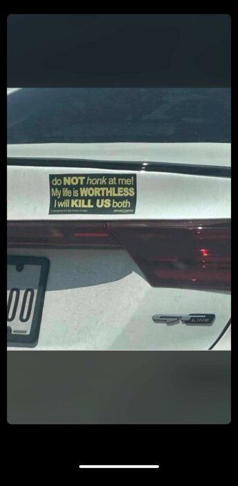 Bilens bakdel med ett klistermärke som varnar för att tuta, med humoristiskt hotfullt budskap.