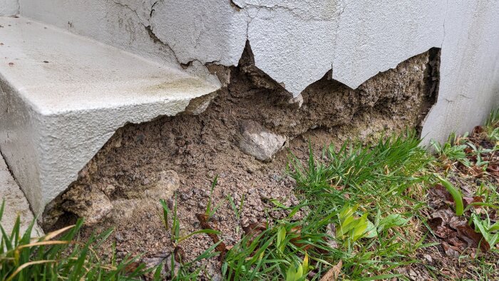 Skadad betongtrappa med stora sprickor och avbrutna delar vid basen mot gräs och jord.