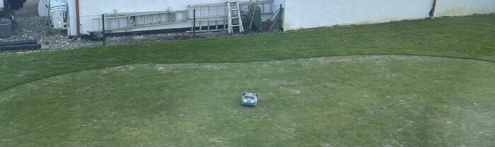 Robotgräsklippare klipper en gräsmatta med ojämn grästillväxt och vissa skadade områden.