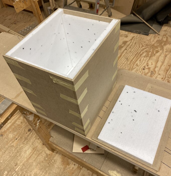 Hemmagjord isolerad låda av MDF och cellplast med tejpade kanter och lös lockdel, på ett verkstadsbord.