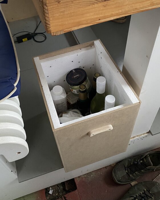 Hemmagjord isolerad kylväska i MDF och cellplast med flaskor och kylklampar, står på ett däck.