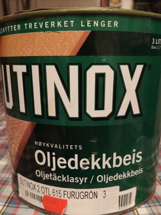 En grön och brun burk med texten "BUTINOX Oljedekkbeis" som används för träskyddsbehandling.