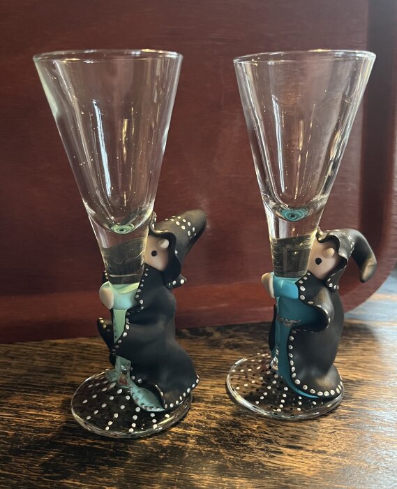 Två dekorativa glas champagneglas med figurer som stjälkgrepp på en mörkt träbakgrund.