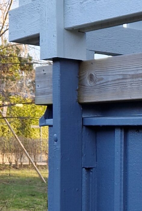Detalj av husets blå entré med ett grått trästaket fastsatt vid en pelare, som visar stabilitet och konstruktion.