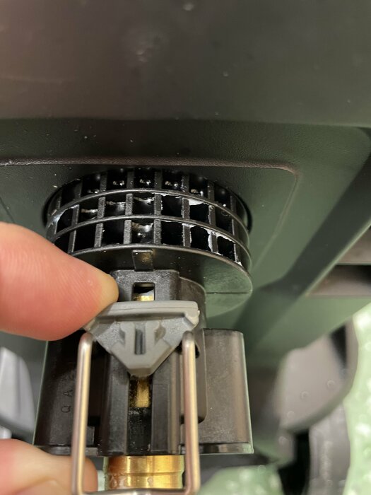 En hand som trycker på en grå plastbit vid en mässingsdel i en maskin, vilket exponerar ett litet hål.